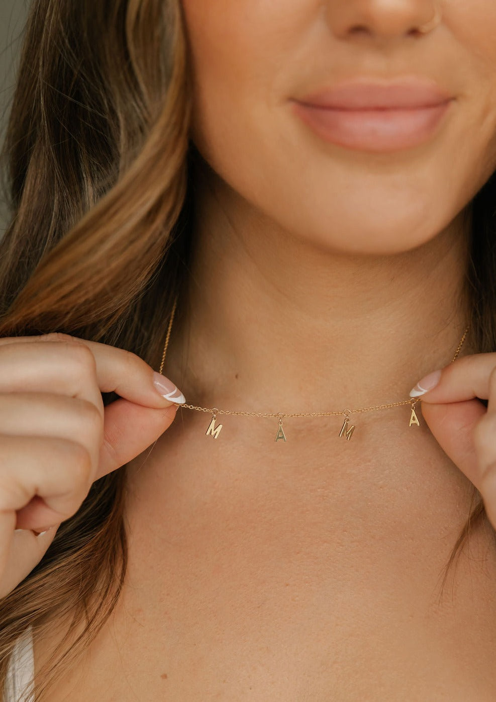 a woman is wearing a mama letter necklace