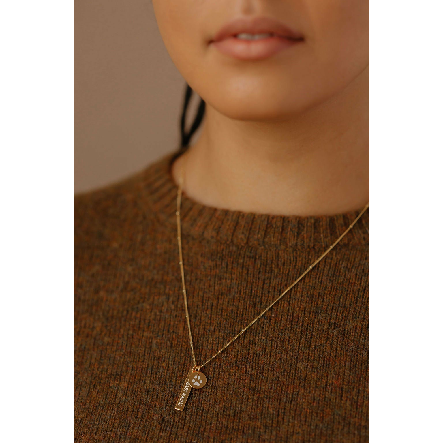 a women is wearing a paw print coin charm and a signature bar pendant necklace. 