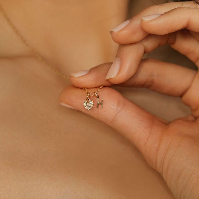 a woman is holding the diamond heart initial gold pendant necklace.