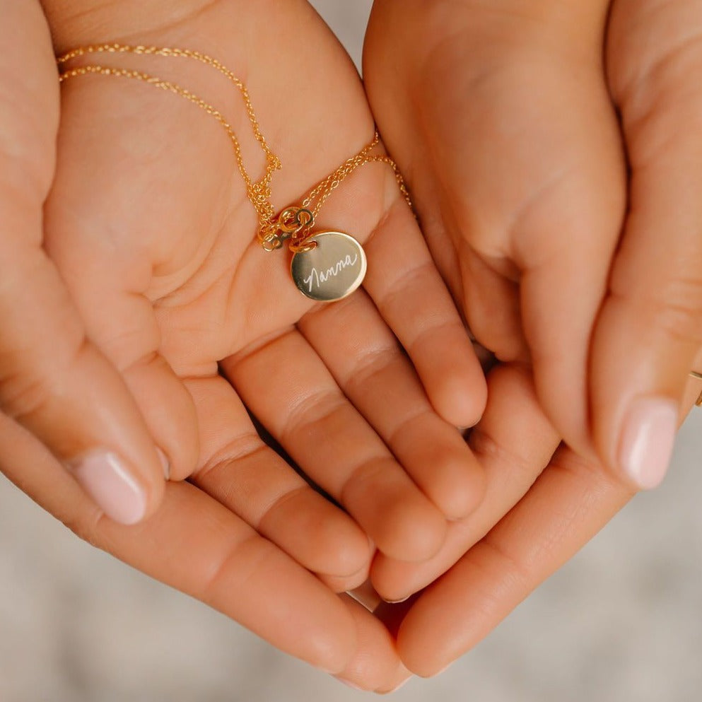 mother and daughter holding a handwriting coin necklace with the word Nanna in handwriting.