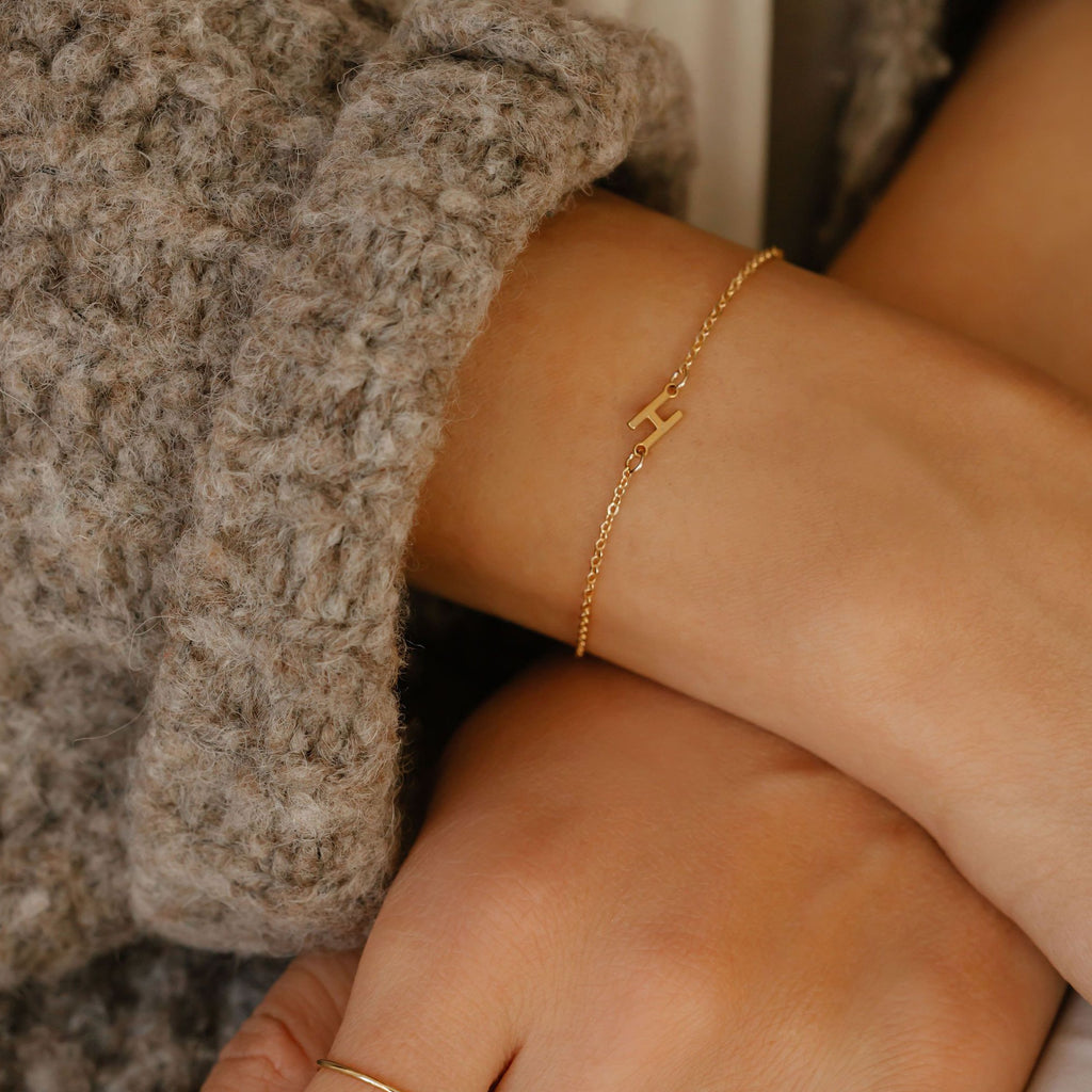 a women is wearing a sideways initial letter bracelet with the letter H